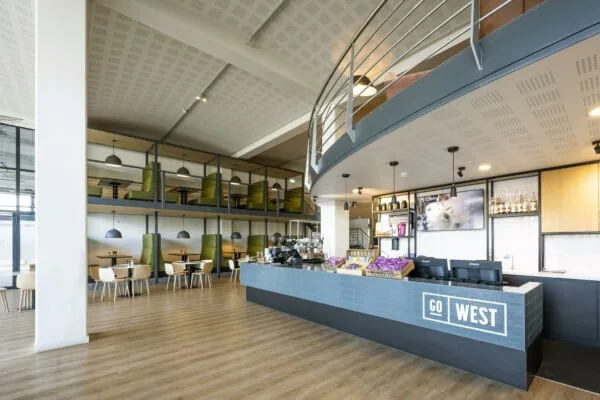 Moderne horecaruimte met een koffiebar genaamd GO WEST en zitgelegenheid op twee niveaus aan de Kabelweg.