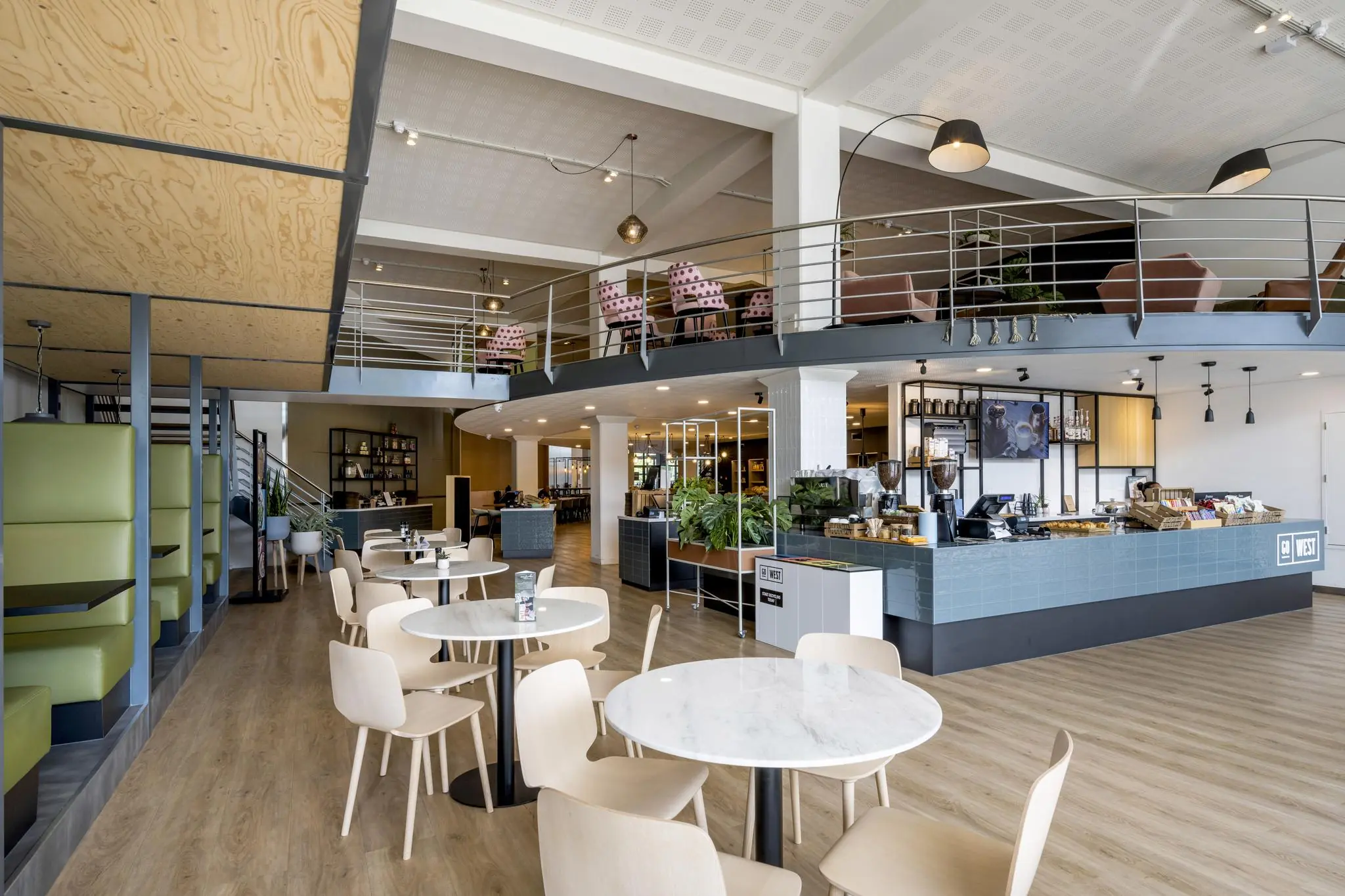 Modern ingerichte lunchroom aan de Kabelweg met een open mezzanine, lichte houten meubels en een koffiebar.