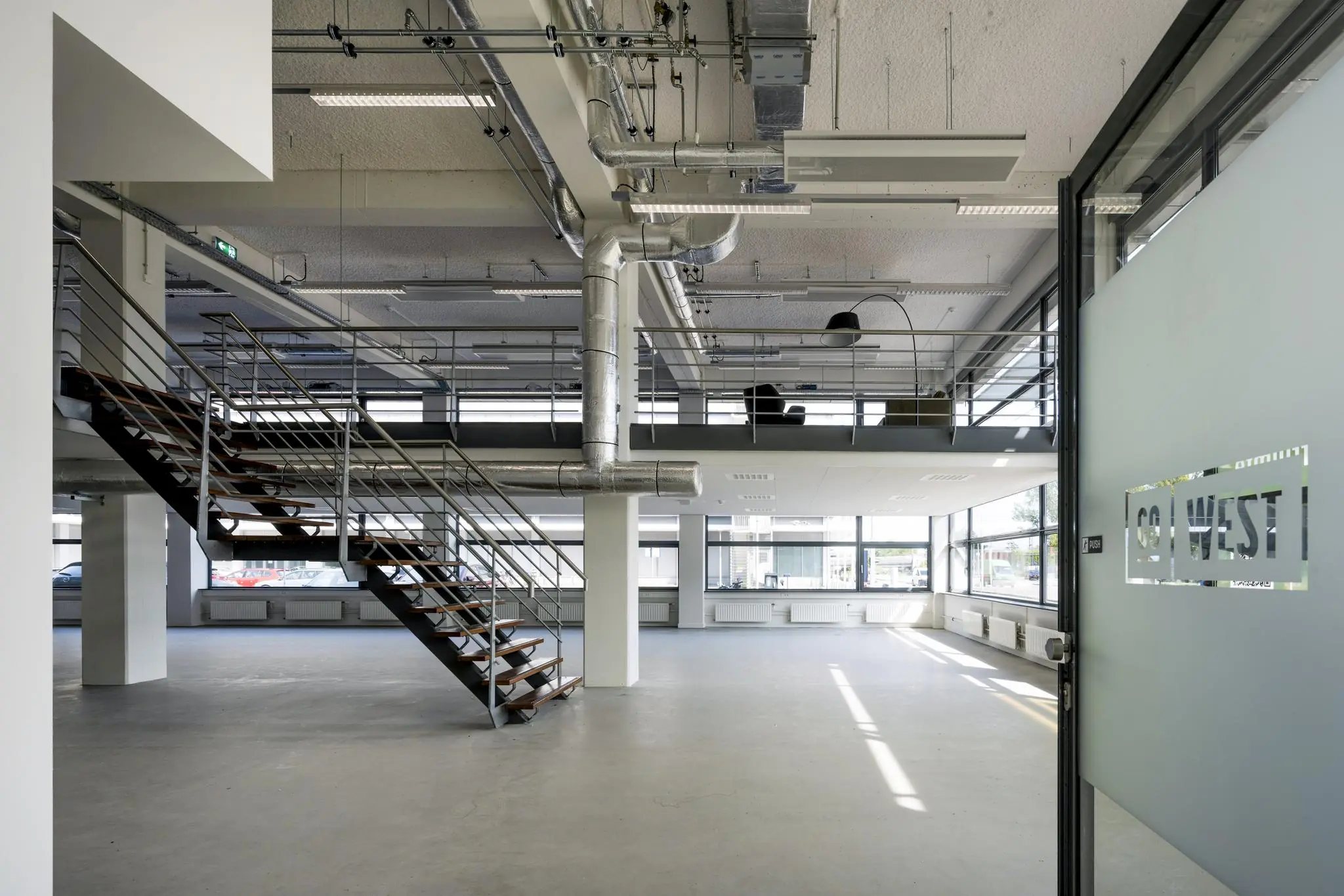 Moderne, industriële kantoorruimte aan de Kabelweg met een open trap, grote ramen en zicht op de entree met CO-WEST logo op de deur.