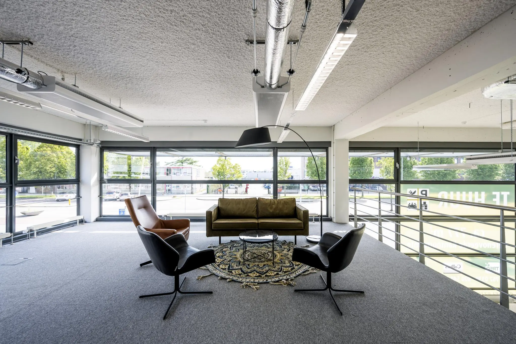 Moderne zitruimte op een kantoor aan de Kabelweg met een bank, stoelen, kleed en grote ramen met uitzicht op de straat.