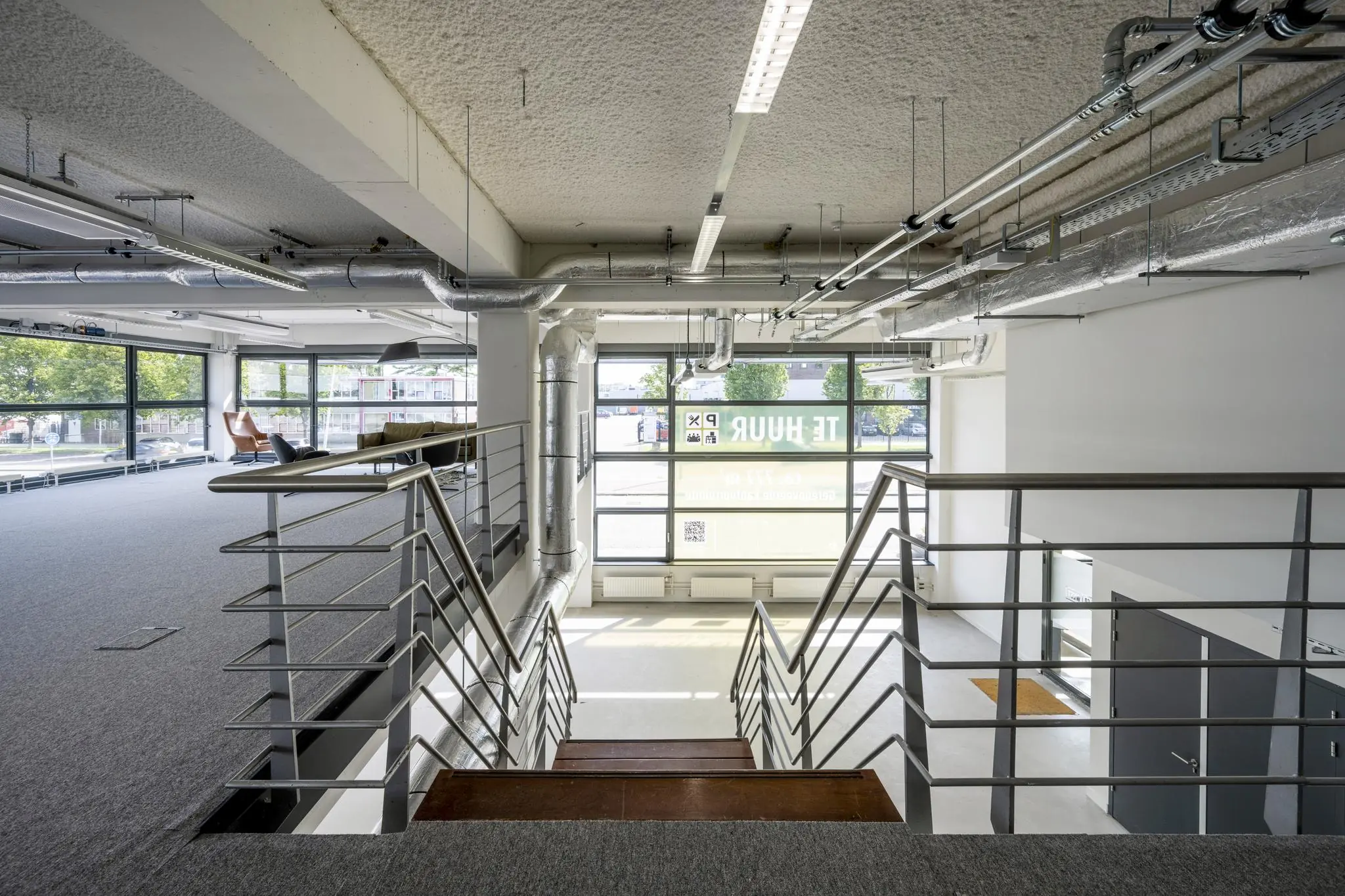 Moderne kantoorruimte aan de Kabelweg met grote ramen, zicht op een trap en industrieel plafond.