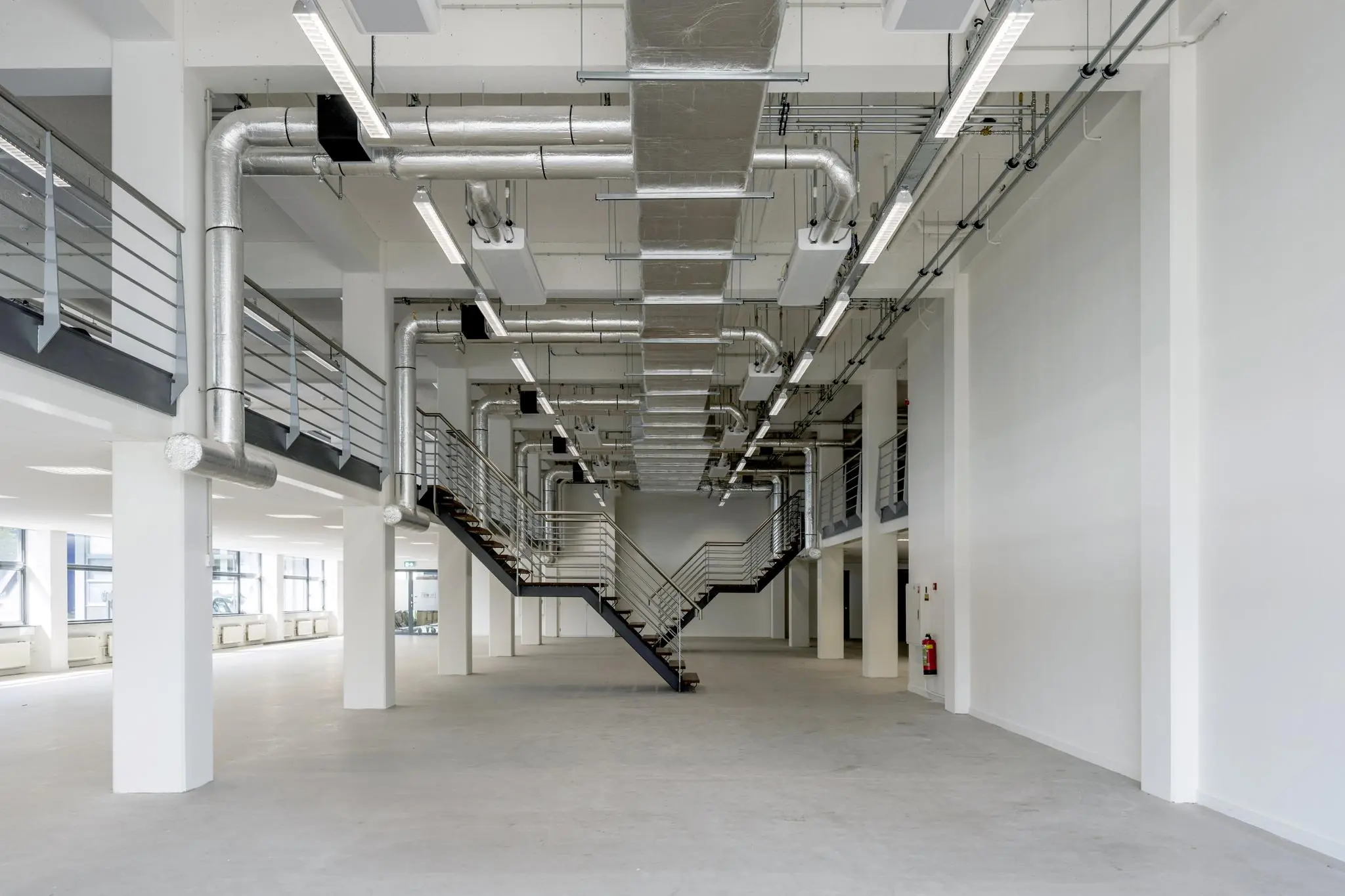 Moderne, industriële kantoorruimte aan de Kabelweg met een centrale trap en zichtbare luchtkanalen.