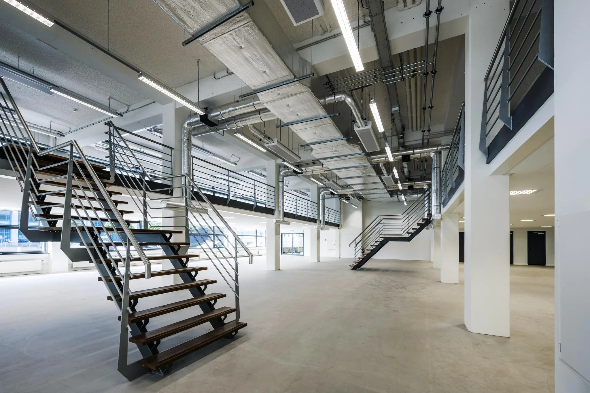 Moderne, industriële kantoorruimte aan de Kabelweg met open vloerplan, metalen trappen en zichtbare leidingen.