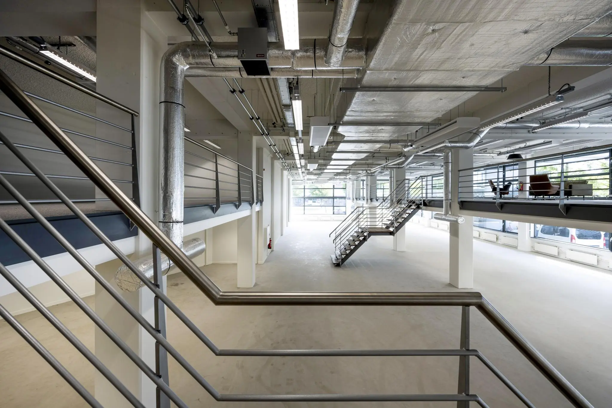 Moderne industriële kantoorruimte aan de Kabelweg met open indeling, stalen trap en zichtbare ventilatiebuizen.