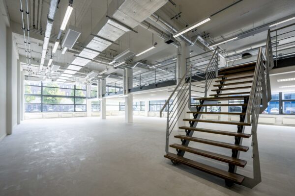 Moderne, industriële kantoorruimte aan de Kabelweg met open indeling, grote ramen en een metalen trap.