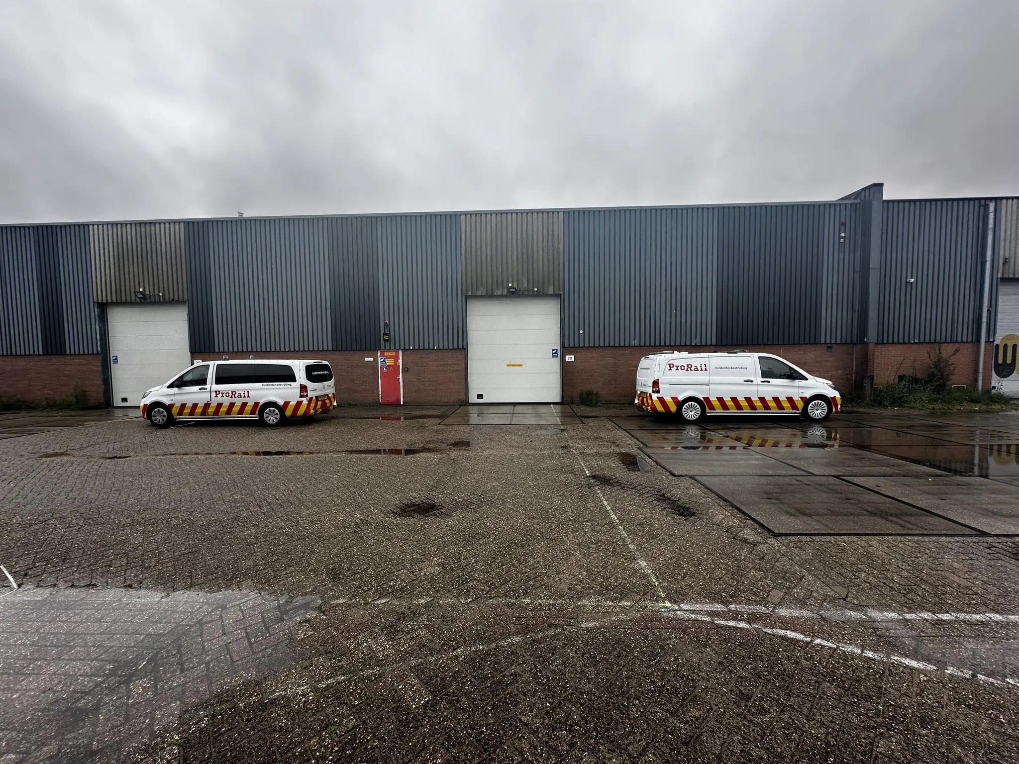 Twee ProRail-busjes staan geparkeerd voor een industrieel gebouw aan de Locomotiefstraat op een regenachtige dag.