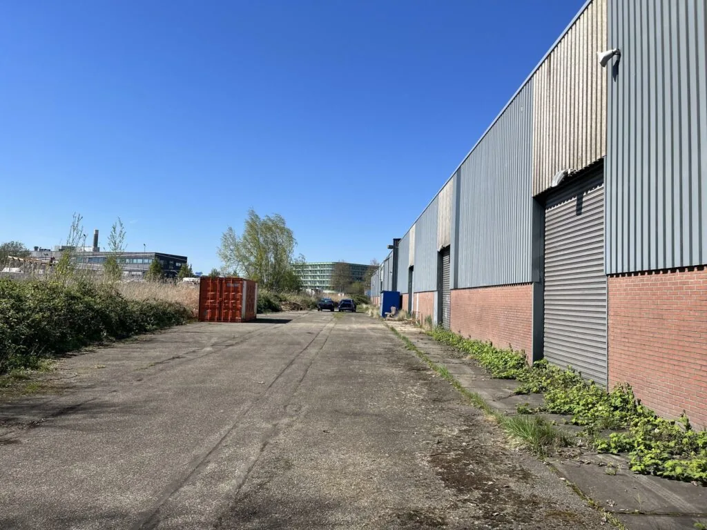 Industrieel terrein aan de Locomotiefstraat met loods, geparkeerde auto's en een rode container langs een asfaltweg.