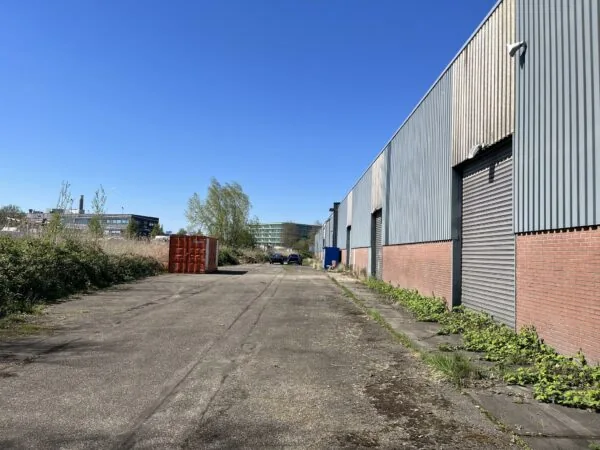 Industrieel terrein aan de Locomotiefstraat met loods, geparkeerde auto's en een rode container langs een asfaltweg.
