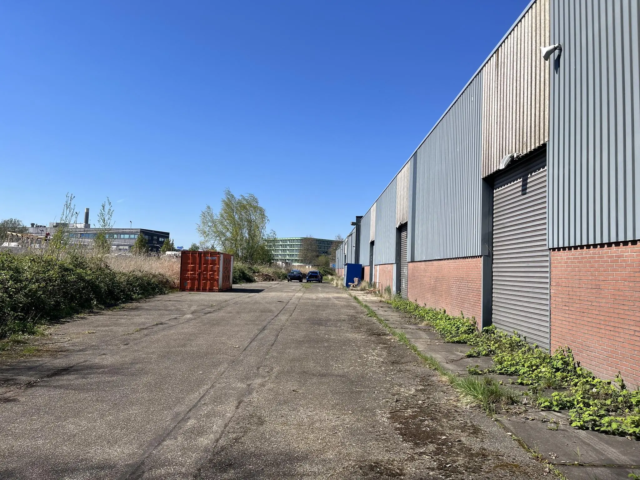 Industrieel terrein aan de Locomotiefstraat met loods, geparkeerde auto's en een rode container langs een asfaltweg.