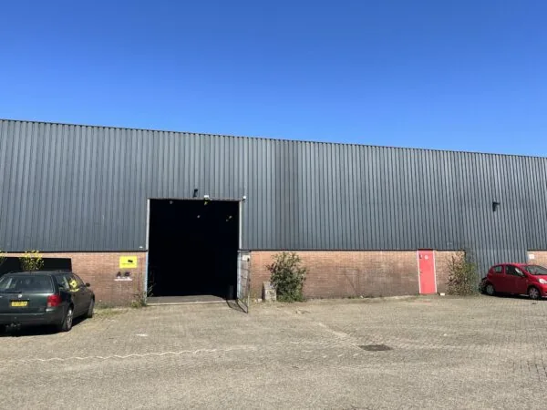 Vooraanzicht van een bedrijfsloods aan de Locomotiefstraat met geopende ingang en twee geparkeerde auto’s ervoor.