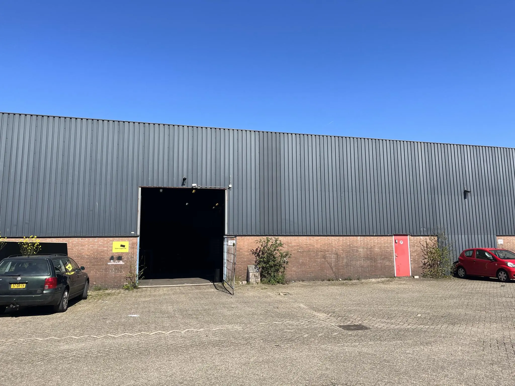 Vooraanzicht van een bedrijfsloods aan de Locomotiefstraat met geopende ingang en twee geparkeerde auto’s ervoor.