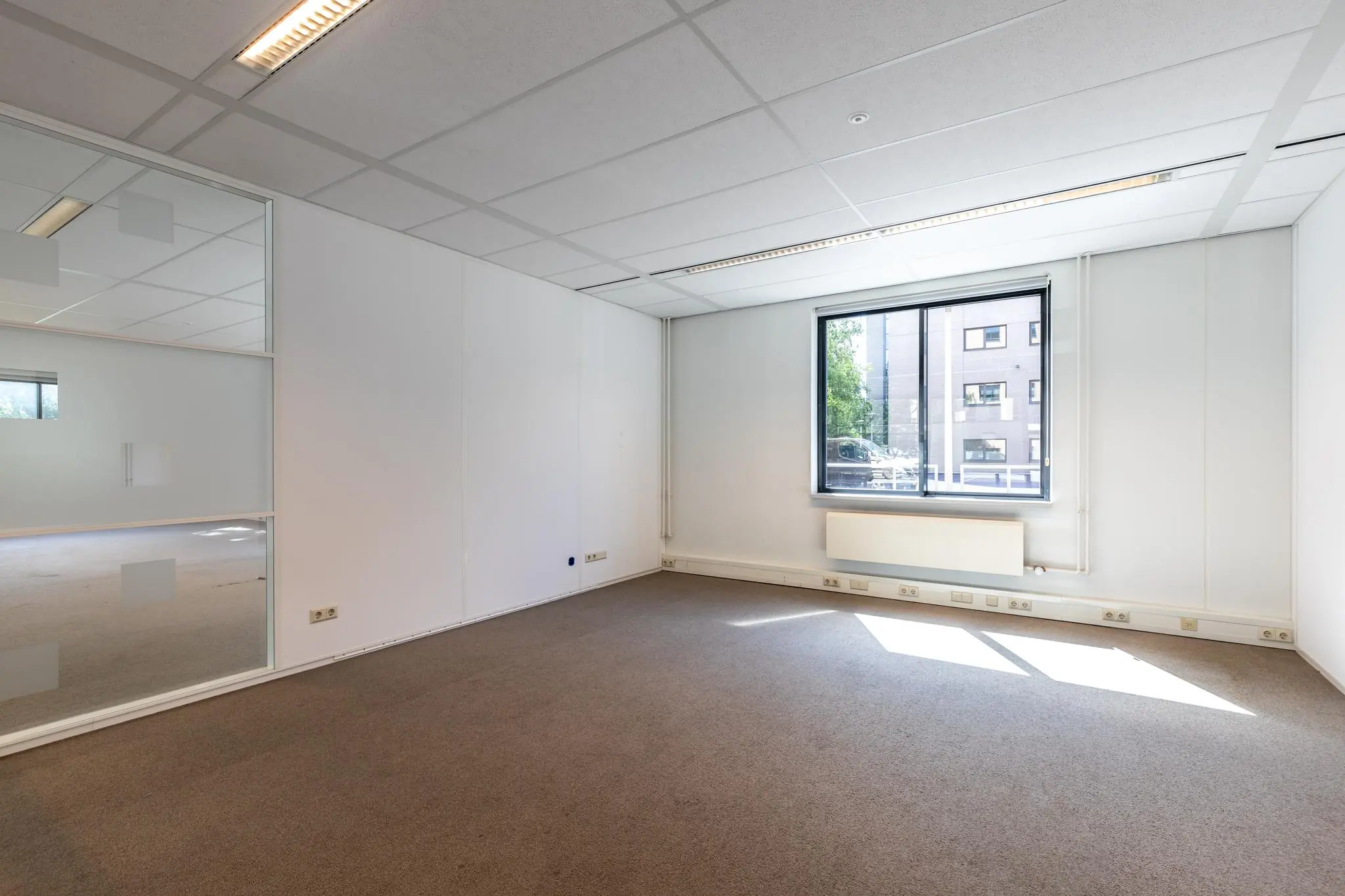 Lichte, lege kantoorruimte aan de Euclideslaan met groot raam en systeemplafond.