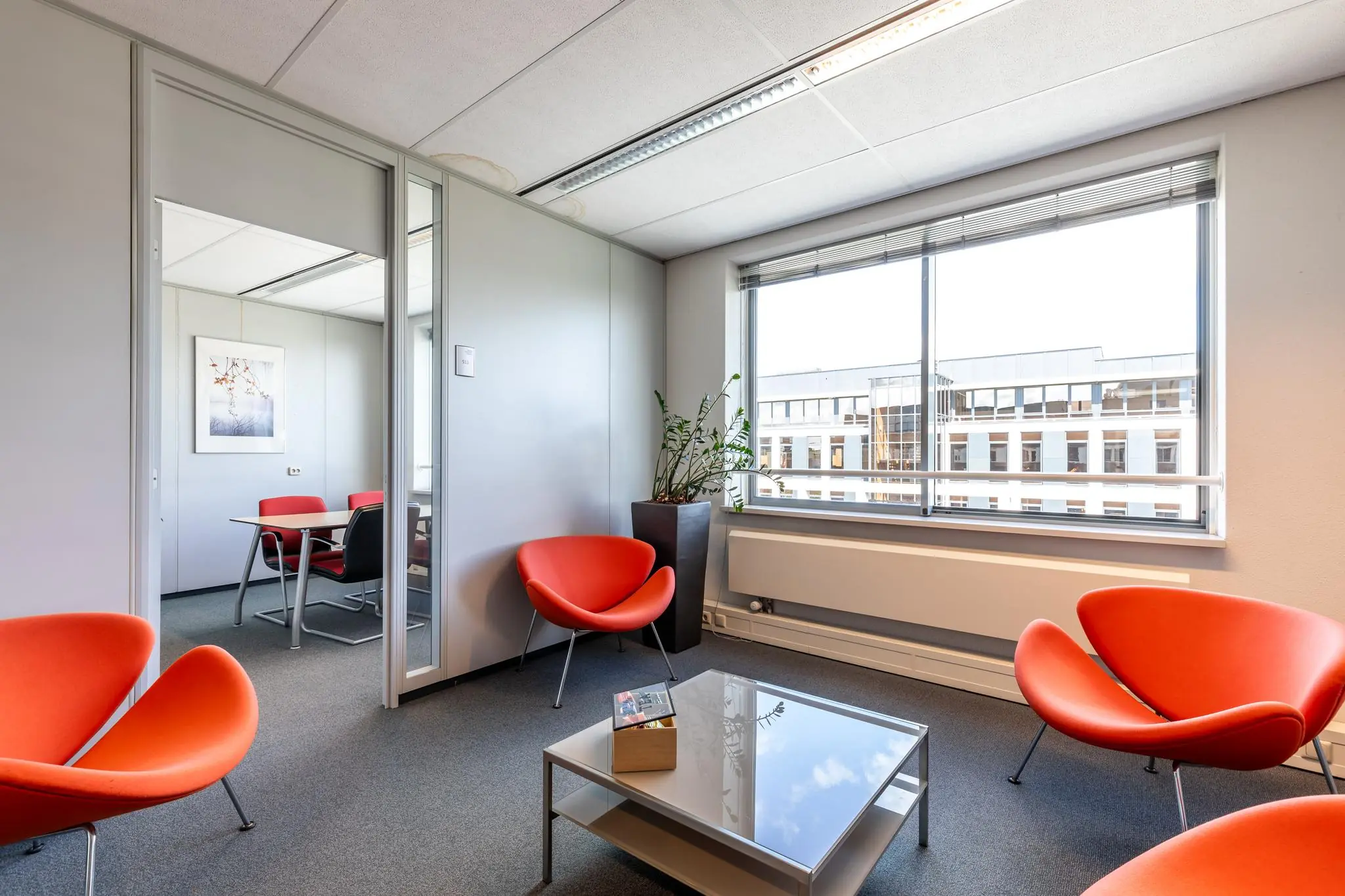 Moderne wachtruimte met feloranje stoelen, glazen salontafel en uitzicht op kantoorgebouw aan de Euclideslaan.