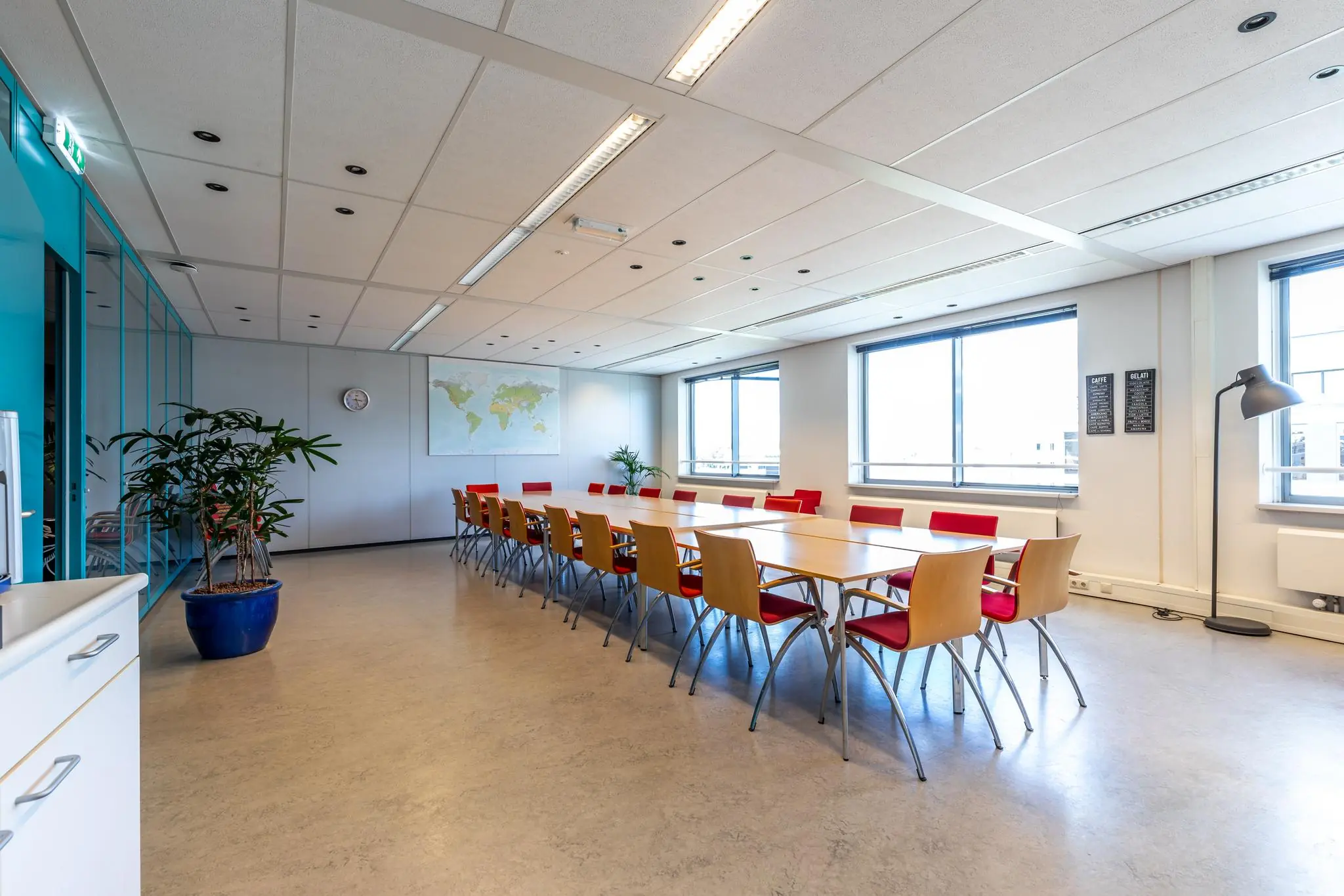 Vergaderruimte aan de Euclideslaan met lange tafel, roodhouten stoelen, grote ramen en een wereldkaart aan de muur.