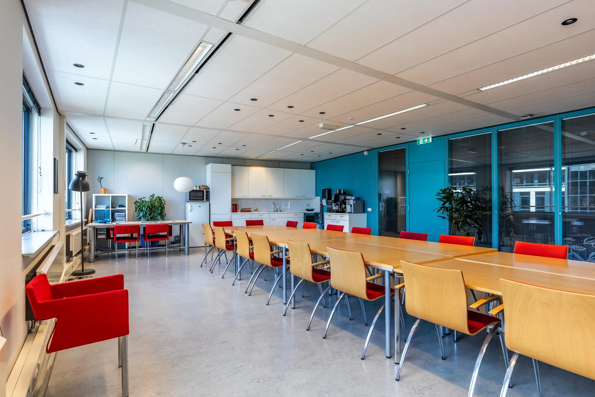Moderne kantoorruimte aan de Euclideslaan met lange vergadertafel, keukenblok en felrode stoelen.