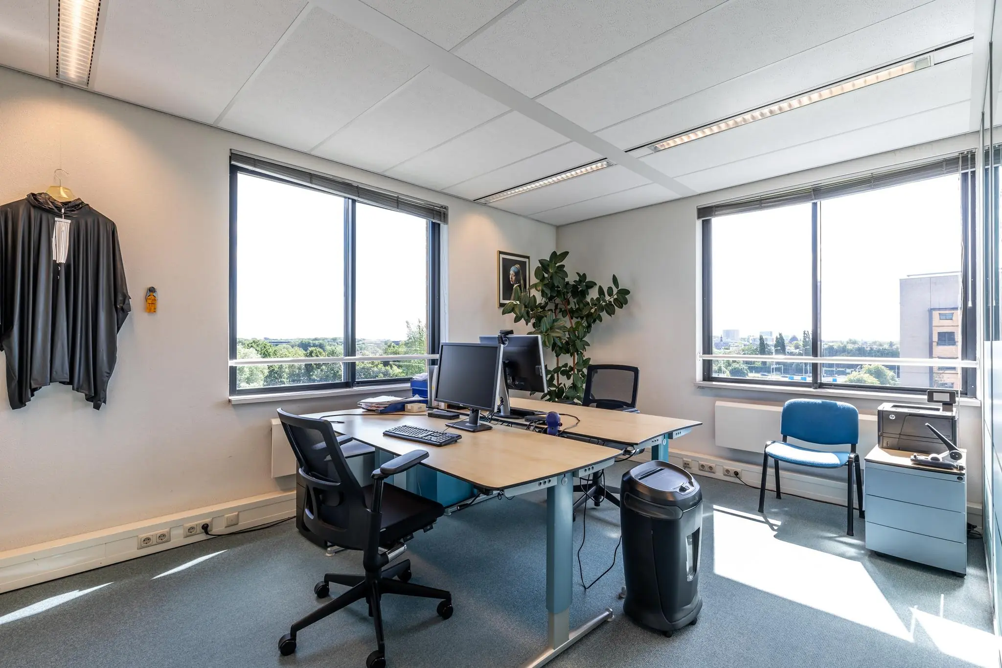 Modern, licht kantoor aan de Euclideslaan met twee werkplekken, uitzicht op groen en een toga aan de muur.