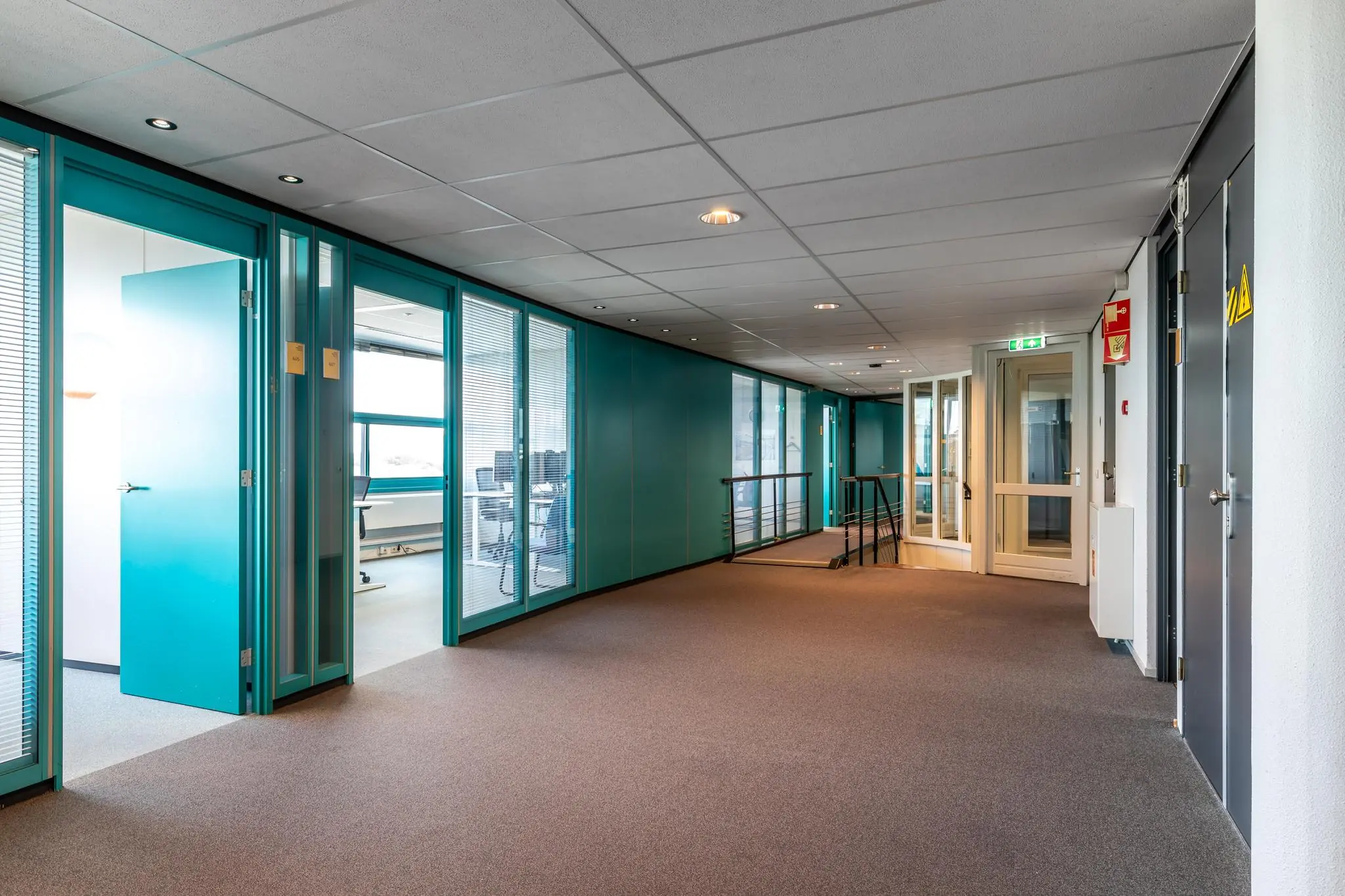 Gang in een modern kantoorgebouw aan de Euclideslaan met glazen kantoorruimtes en turquoise deuren.