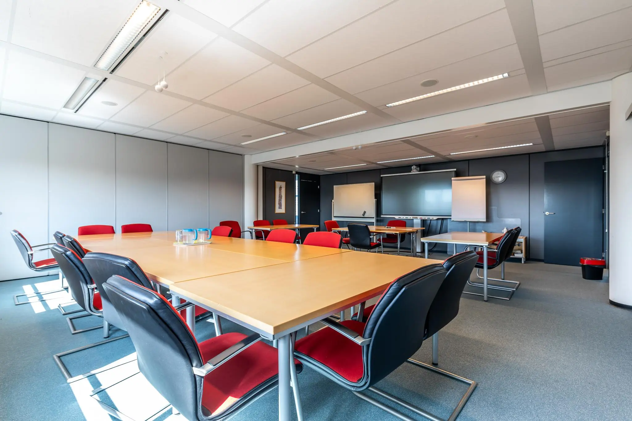 Vergaderruimte met moderne inrichting, houten tafels, rode en zwarte stoelen, en presentatiemiddelen aan de Euclideslaan.