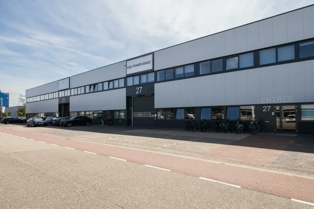 Bedrijfsgebouw aan de Zonnebaan met de ingang van Rad Power Bikes en geparkeerde fietsen en auto’s.