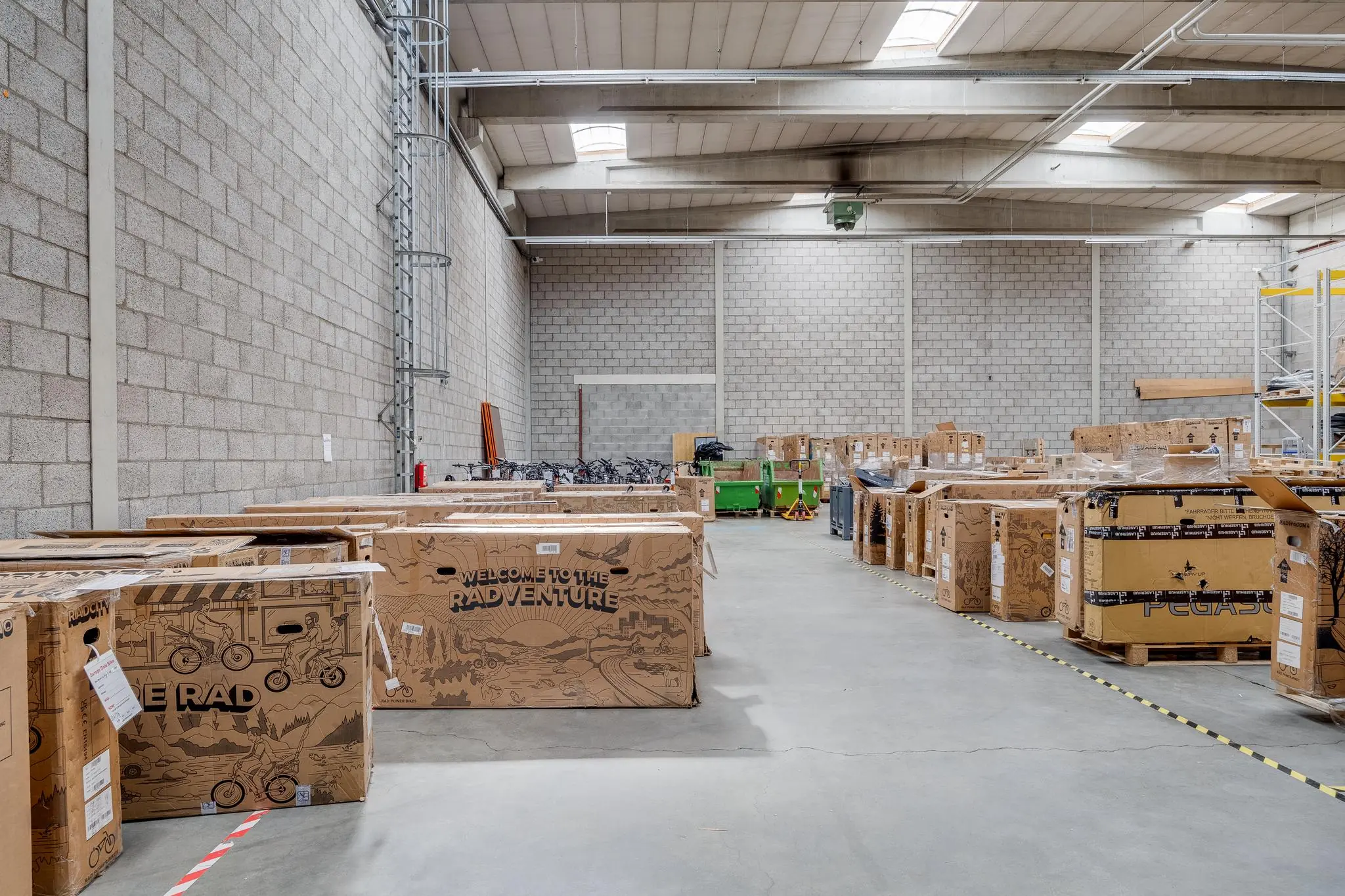 Opslagruimte met grote kartonnen dozen vol fietsen, waaronder exemplaren van het merk Rad Power Bikes.