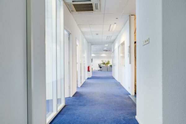Heldere gang in een modern kantoorpand aan de Zonnebaan met blauwe vloerbedekking en witte wanden.