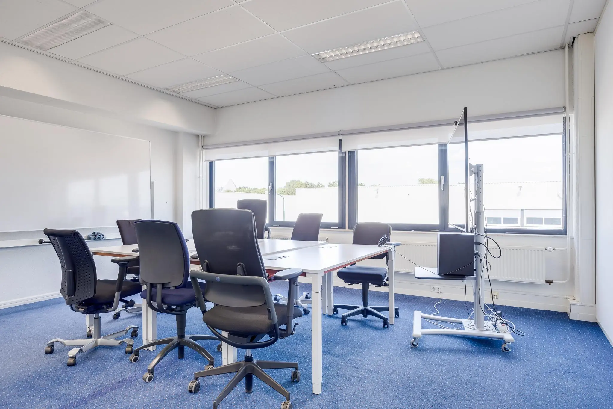 Vergaderruimte op de Zonnebaan met bureaustoelen, tafels, whiteboard en groot beeldscherm bij het raam.