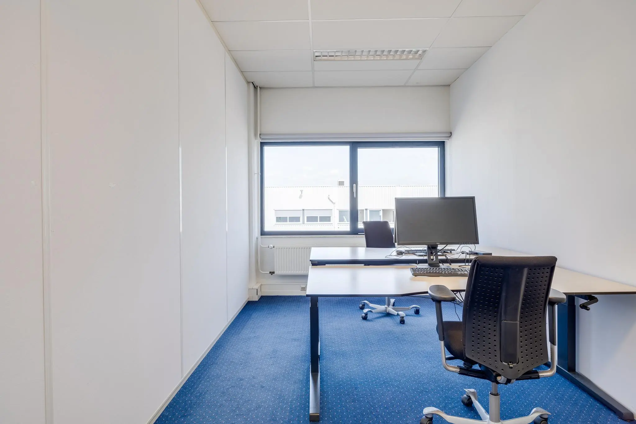 Kleine, lichte kantoorruimte aan de Zonnebaan met twee bureaus, bureaustoelen en een computer.