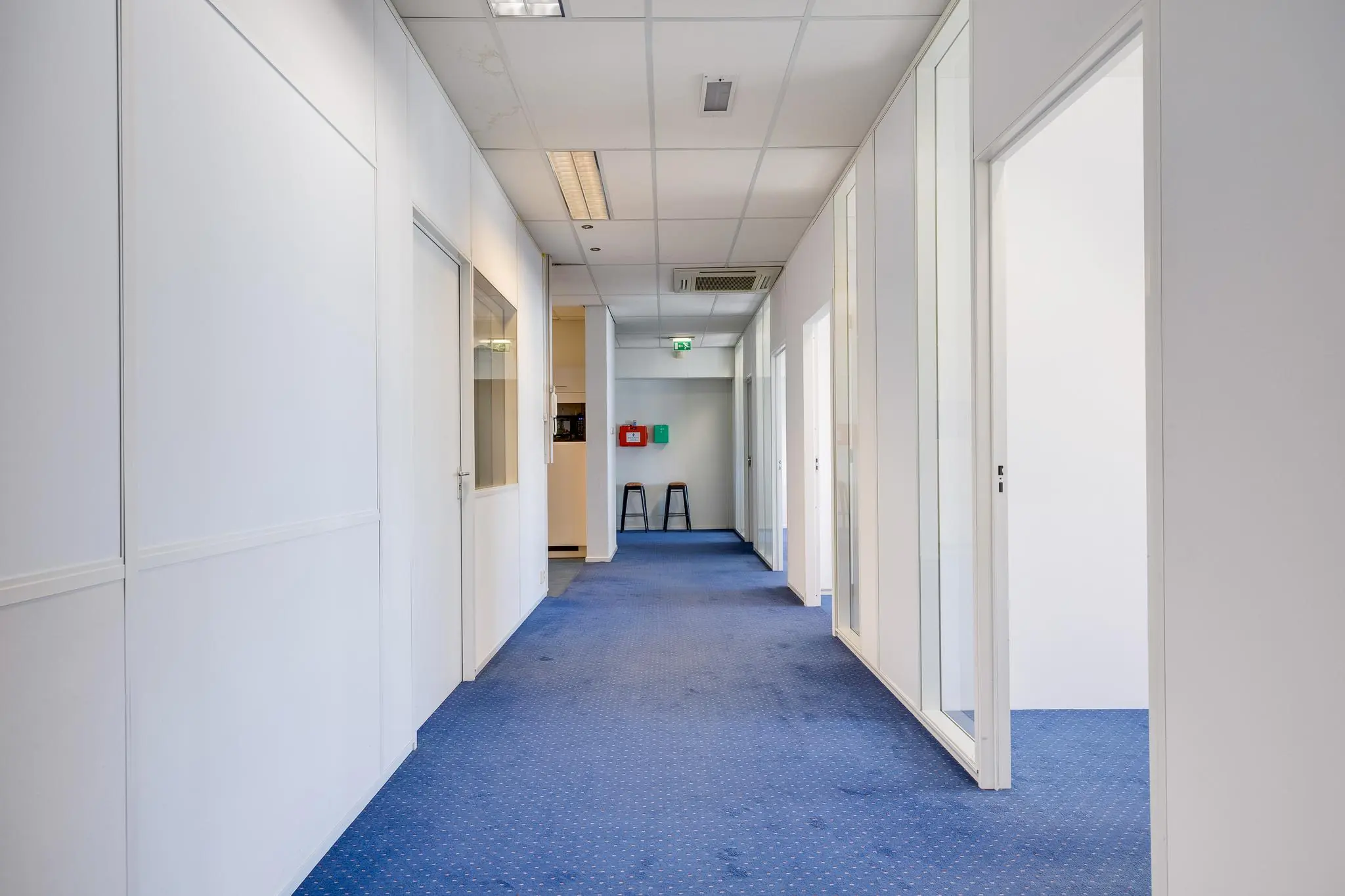 Lichte kantoorruimte aan de Zonnebaan met blauwe vloerbedekking en glazen kantoordeuren.