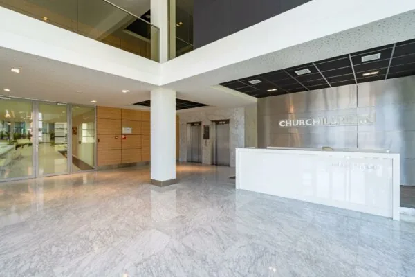 Moderne entreehal van het kantoorgebouw Churchillplein met receptiebalie, liften en glazen vergaderruimte.