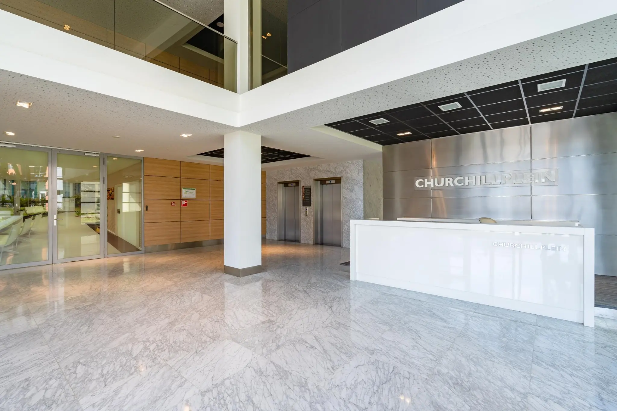 Moderne entreehal van het kantoorgebouw Churchillplein met receptiebalie, liften en glazen vergaderruimte.