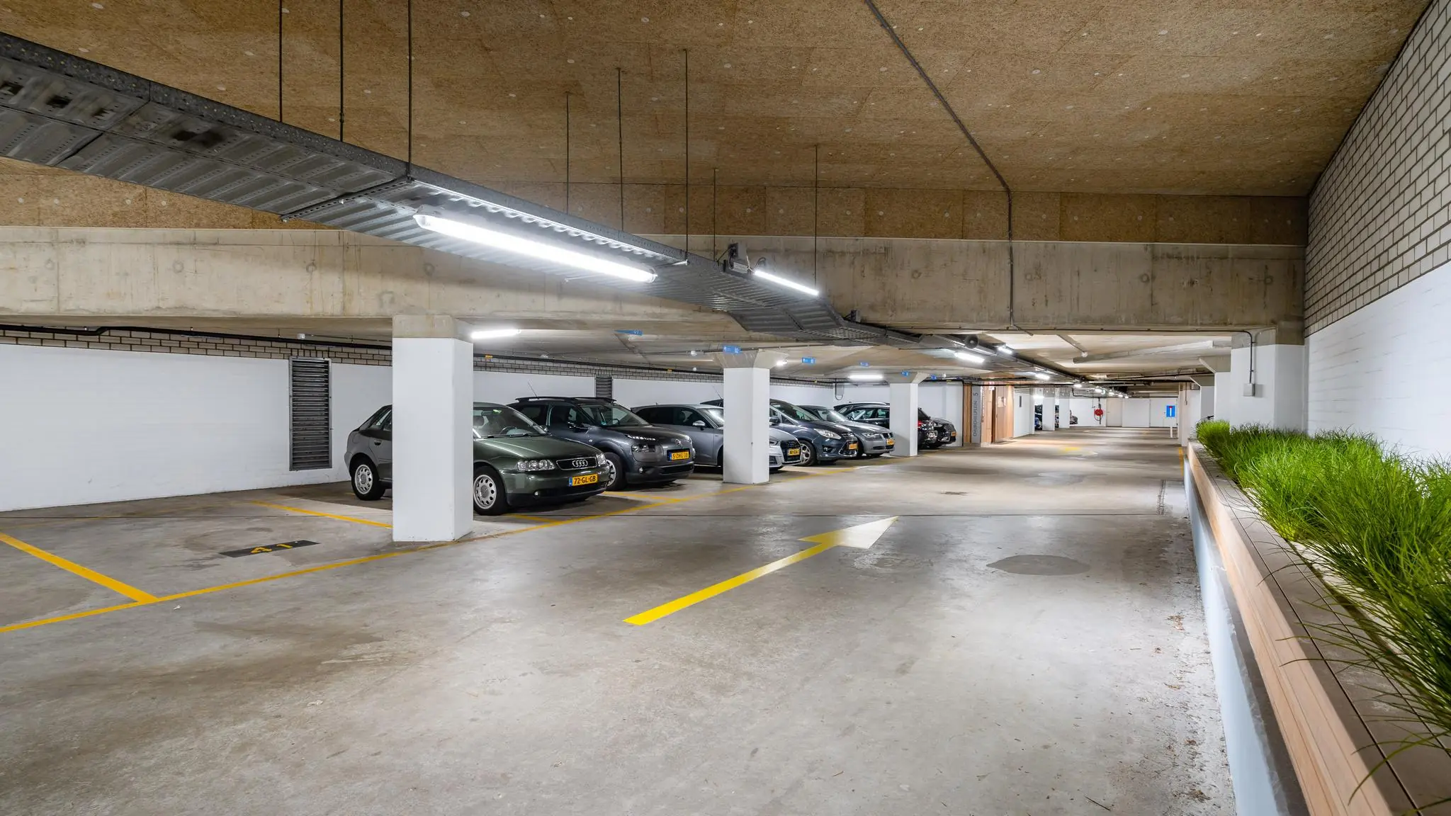 Ondergrondse parkeergarage aan het Churchillplein met geparkeerde auto's en een plantenbak langs de wand.