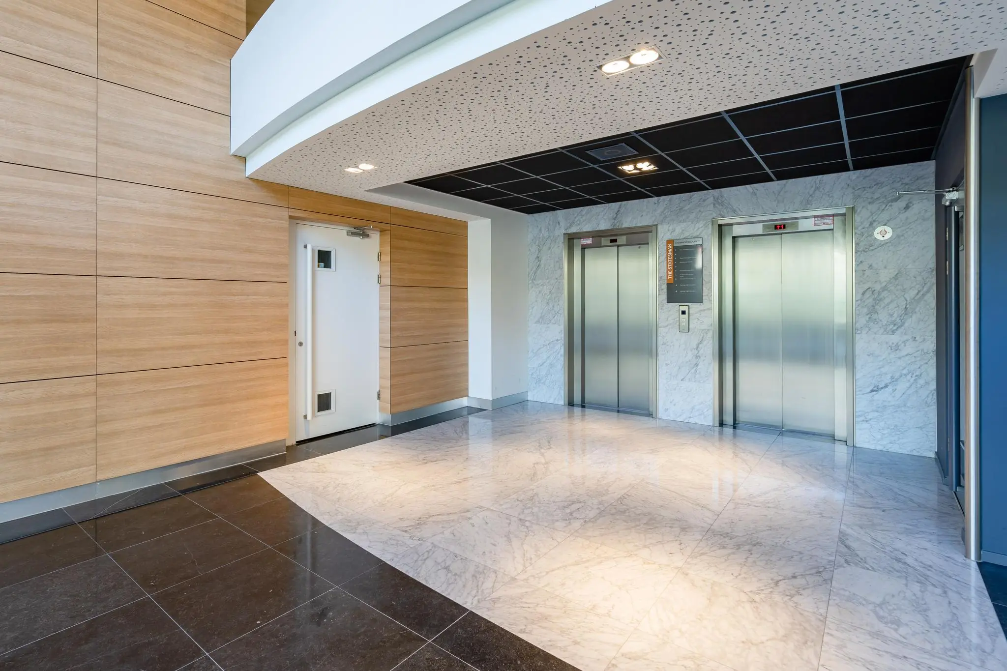 Moderne liftlobby in Churchillplein met twee liften, een witte deur en een strakke afwerking in hout en marmer.