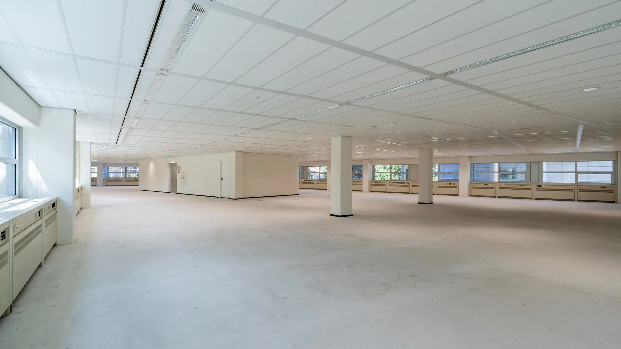 Leeg kantoorpand aan het Churchillplein met witte muren, systeemplafond en grote ramen.