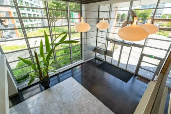 Moderne entreehal van een kantoorpand aan het Churchillplein met grote ramen, hanglampen en een groene plant.