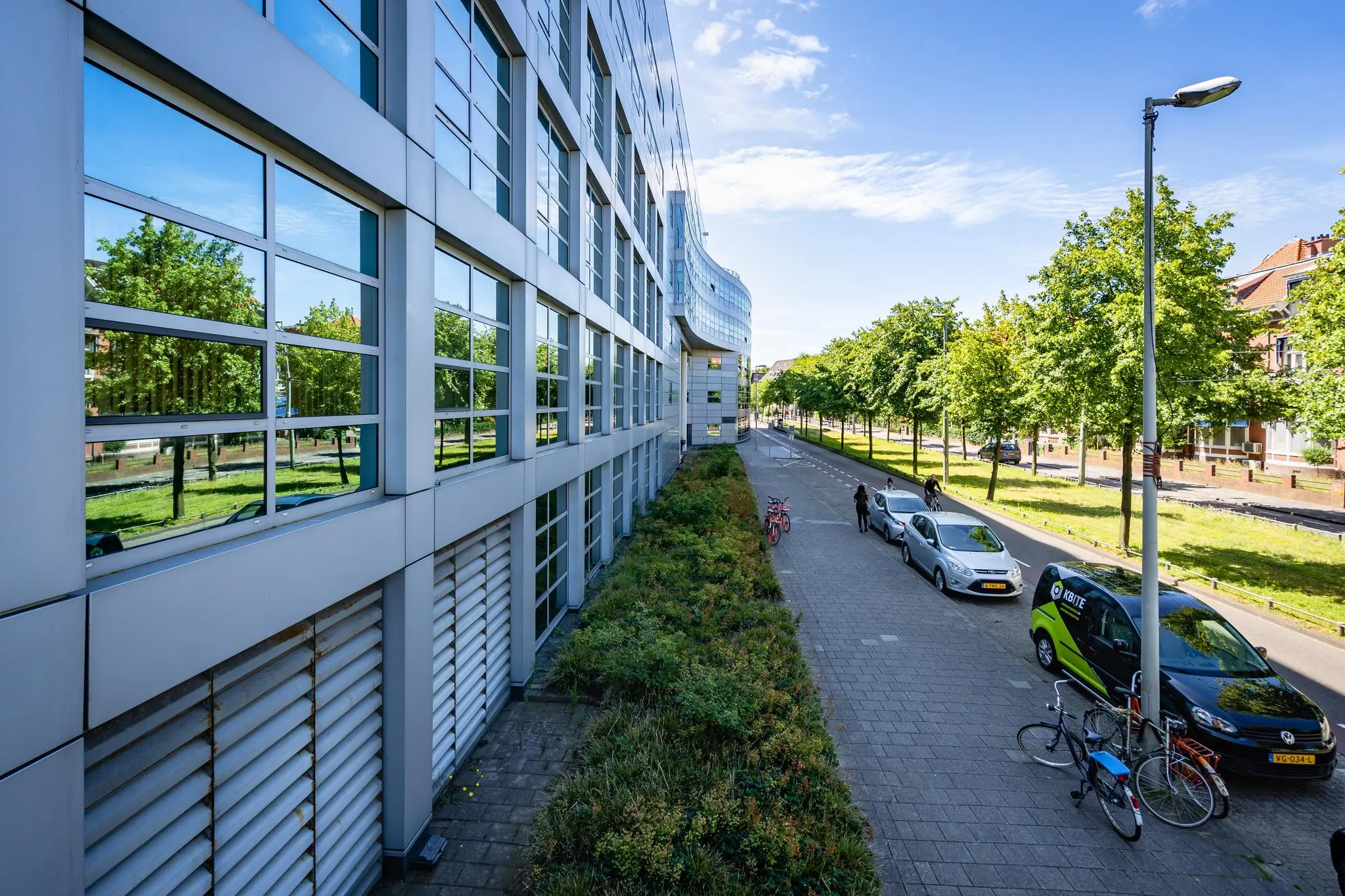 Moderne gevel van een kantoorgebouw aan het Churchillplein met geparkeerde auto's en fietsen langs een boomrijke straat.