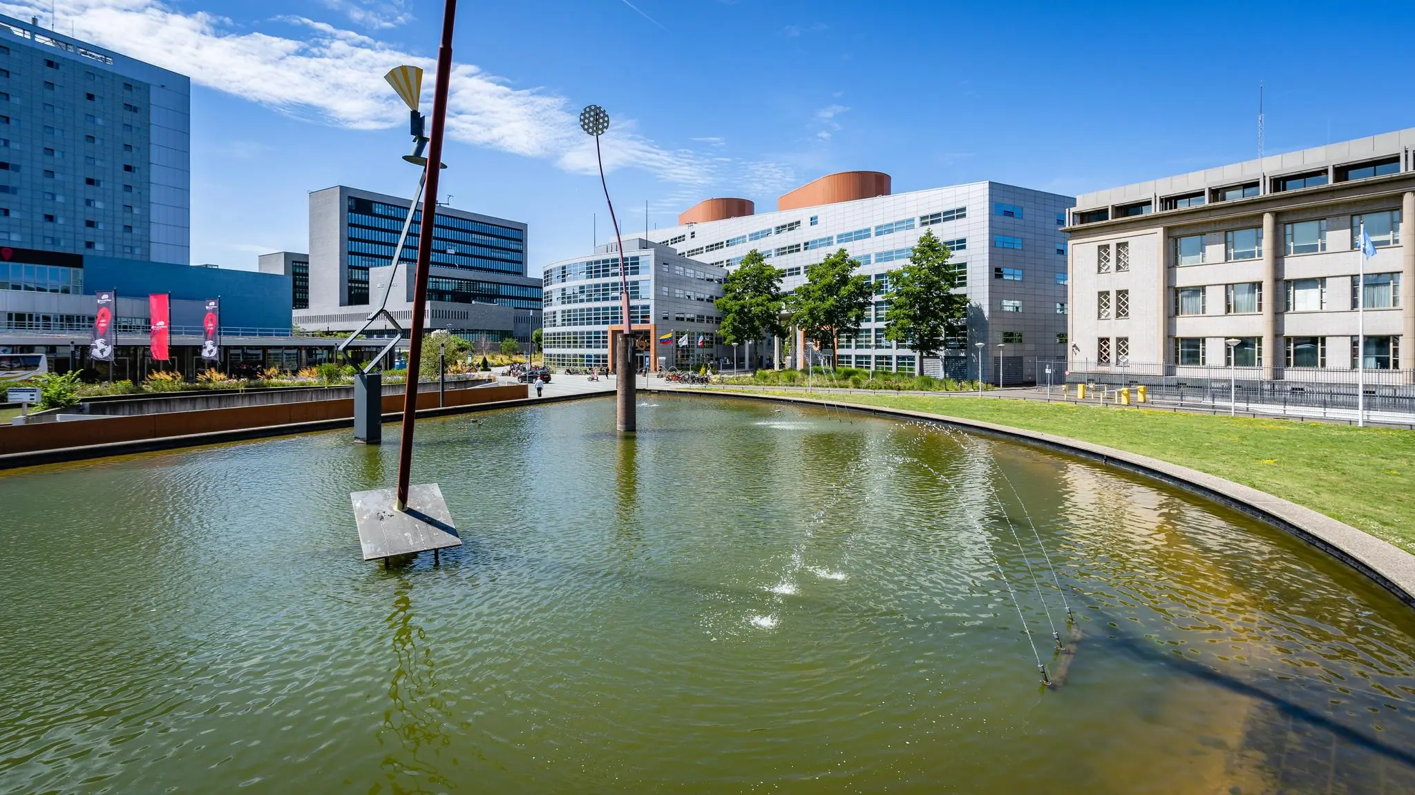 Vijver met moderne kunstobjecten op het Churchillplein in Den Haag, omringd door kantoorgebouwen en een helderblauwe lucht.