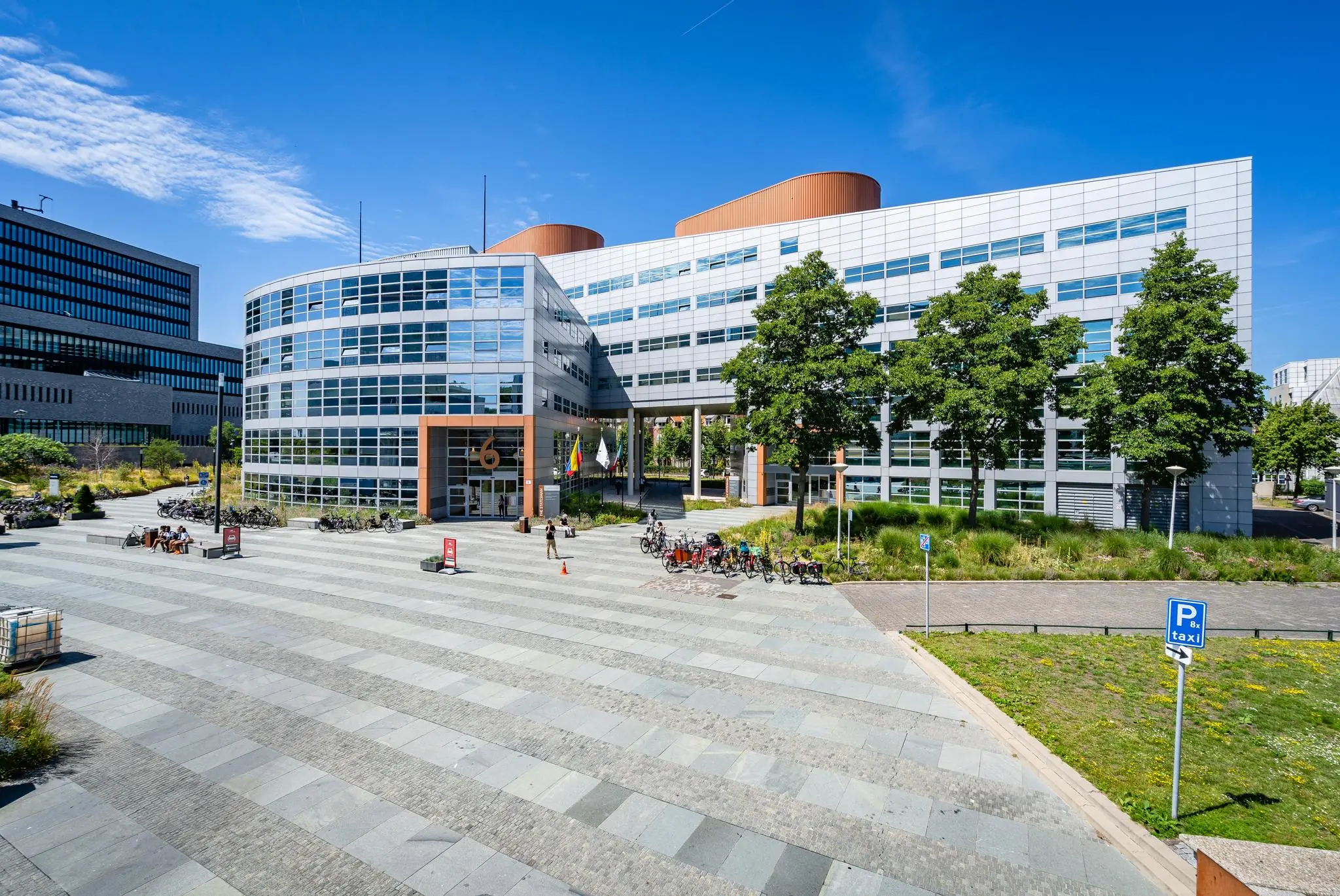 Modern kantoorpand aan het Churchillplein in Den Haag met fietsenrekken, vlaggen en een betegeld plein op de voorgrond.
