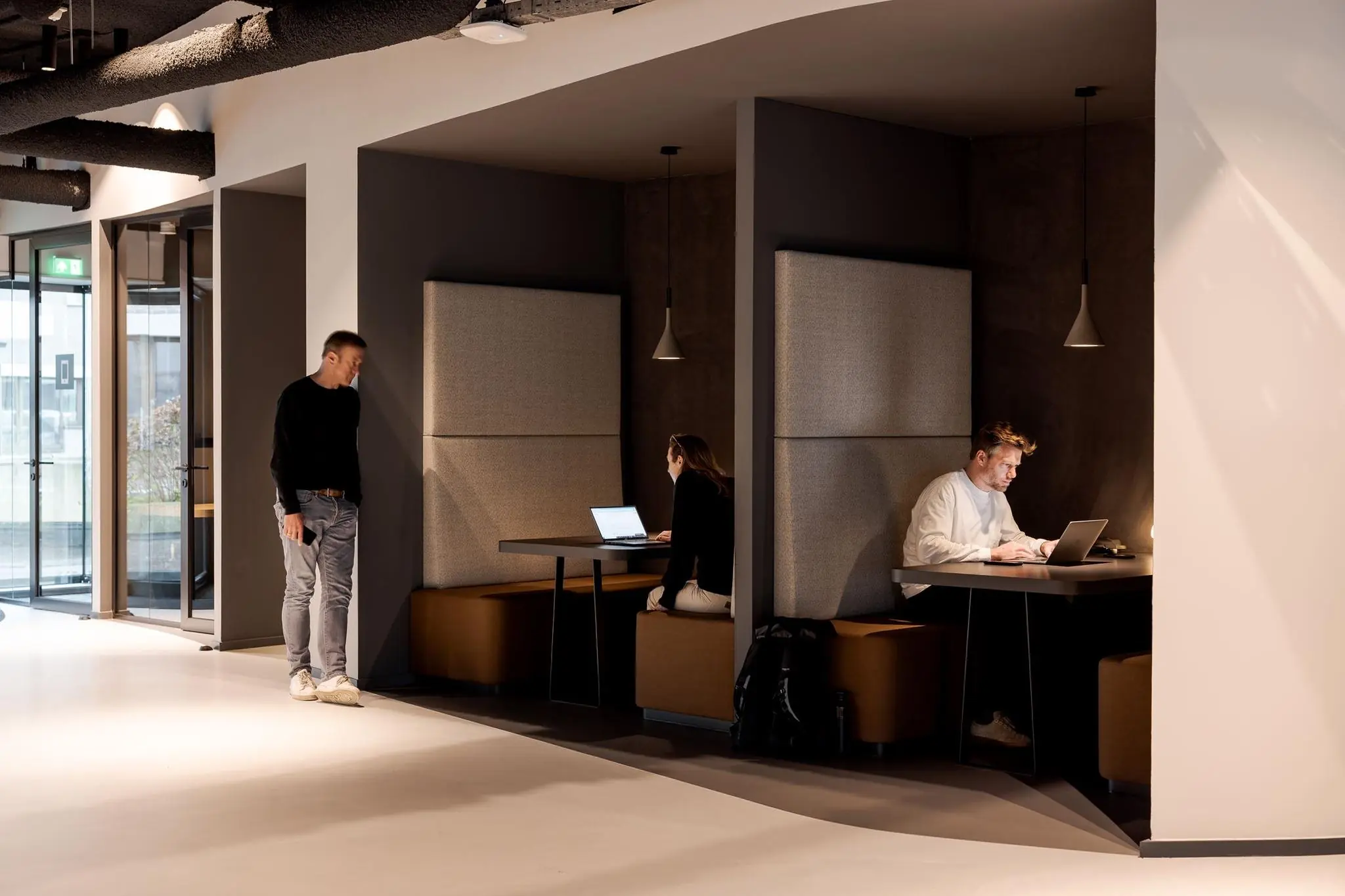 Twee mensen werken op laptops in moderne werkruimtes met zitnissen aan het Weena, terwijl een derde persoon in de gang staat.