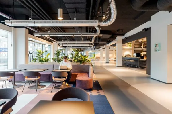 Moderne, open kantoorruimte aan het Weena met zitplekken, veel planten en een persoon die werkt op een laptop.