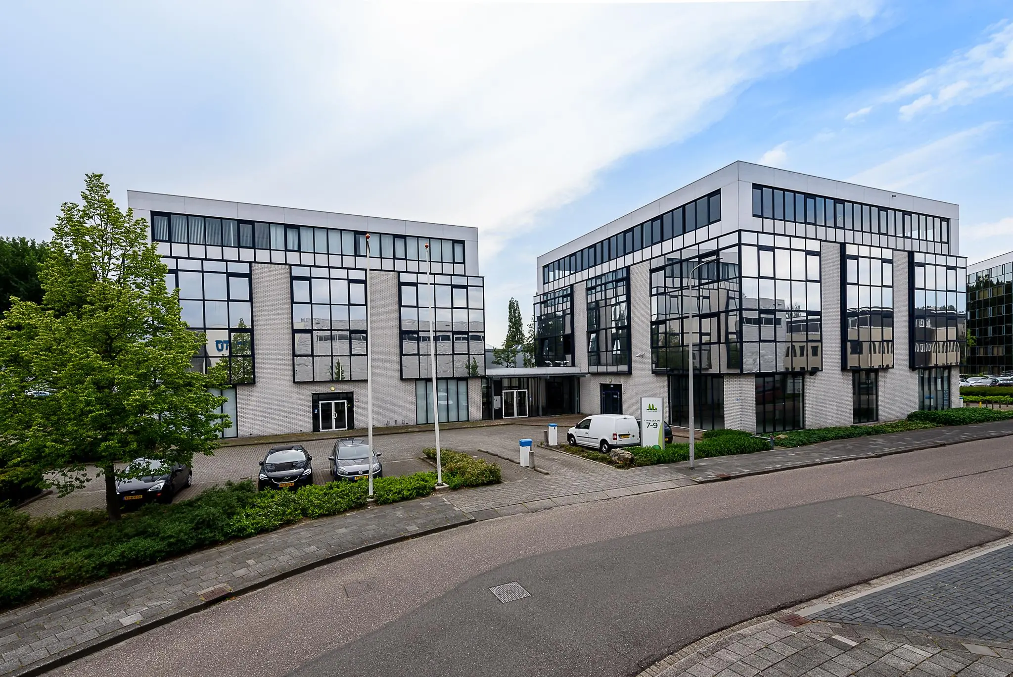 Twee moderne kantoorgebouwen aan de Cypresbaan met grote spiegelramen en een parkeerterrein ervoor.
