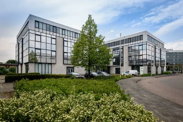 Modern kantoorpand aan de Cypresbaan met grote glazen gevels, omringd door groen en geparkeerde auto's.