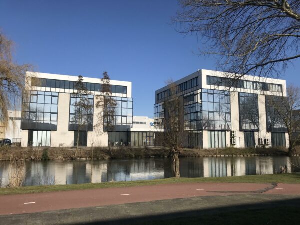 Twee moderne kantoorgebouwen aan de Cypresbaan weerspiegelen in het water op een zonnige dag.