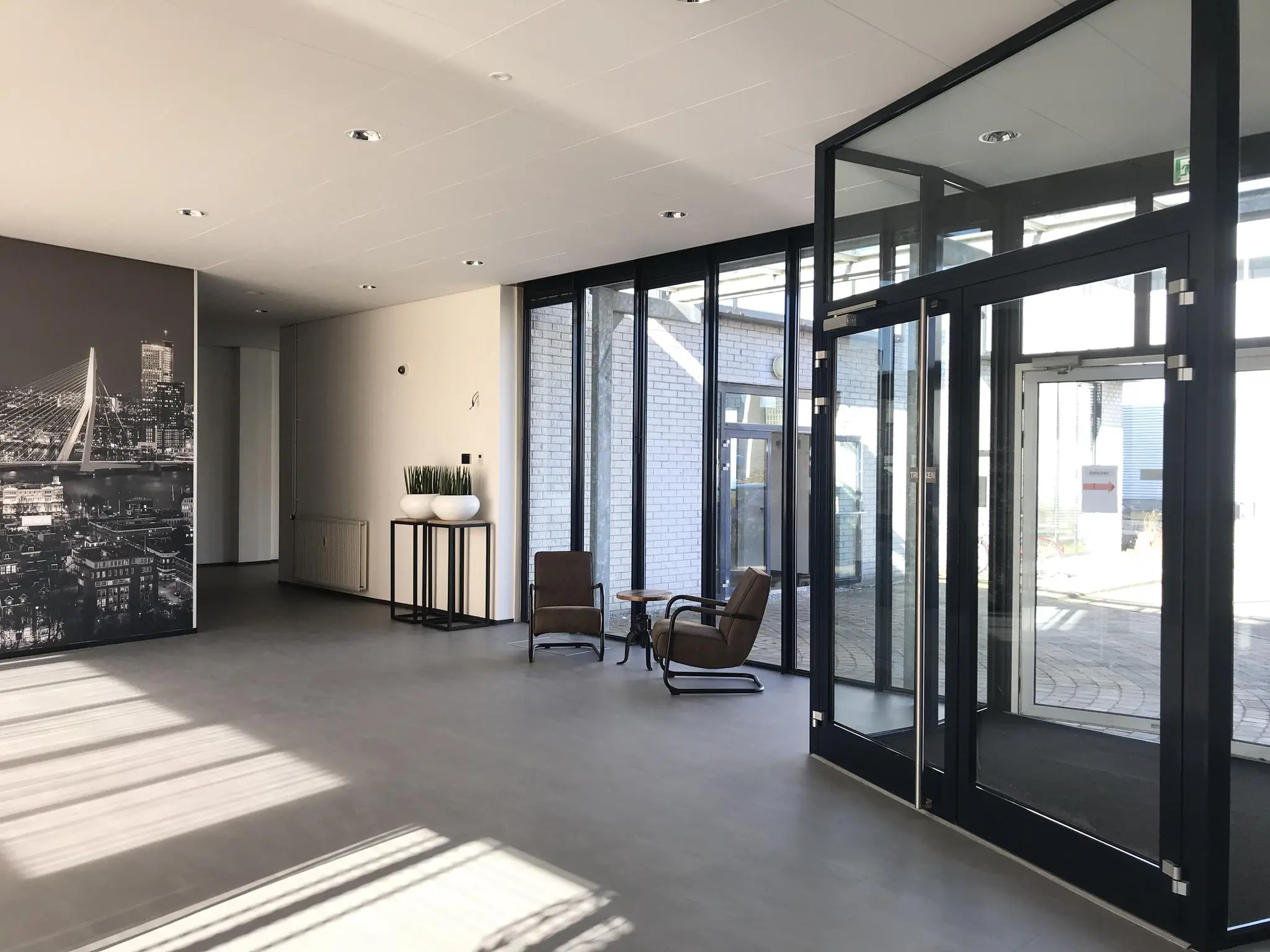 Moderne, lichte entreehal aan de Cypresbaan met glazen deuren, zitgelegenheid en een grote wandfoto van Rotterdam.