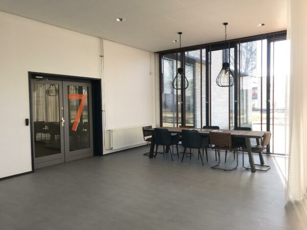 Moderne vergaderruimte aan de Cypresbaan met grote ramen, een houten tafel, en industriële hanglampen.