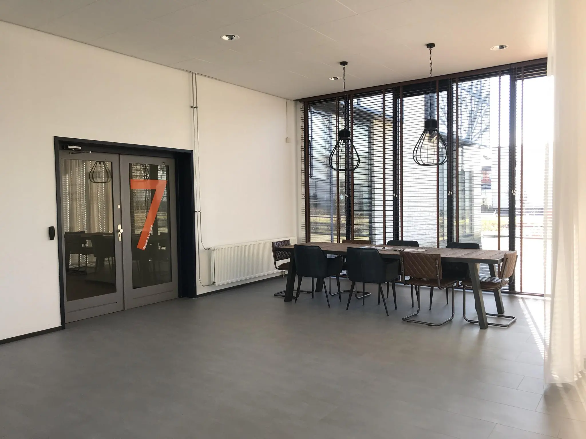 Moderne vergaderruimte aan de Cypresbaan met grote ramen, een houten tafel, en industriële hanglampen.