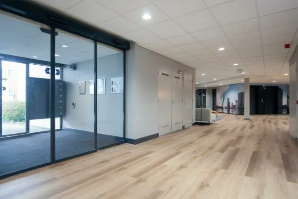 Moderne, lichte entreehal met houten vloer, glazen schuifdeuren en een zithoek, gelegen aan de Cypresbaan.