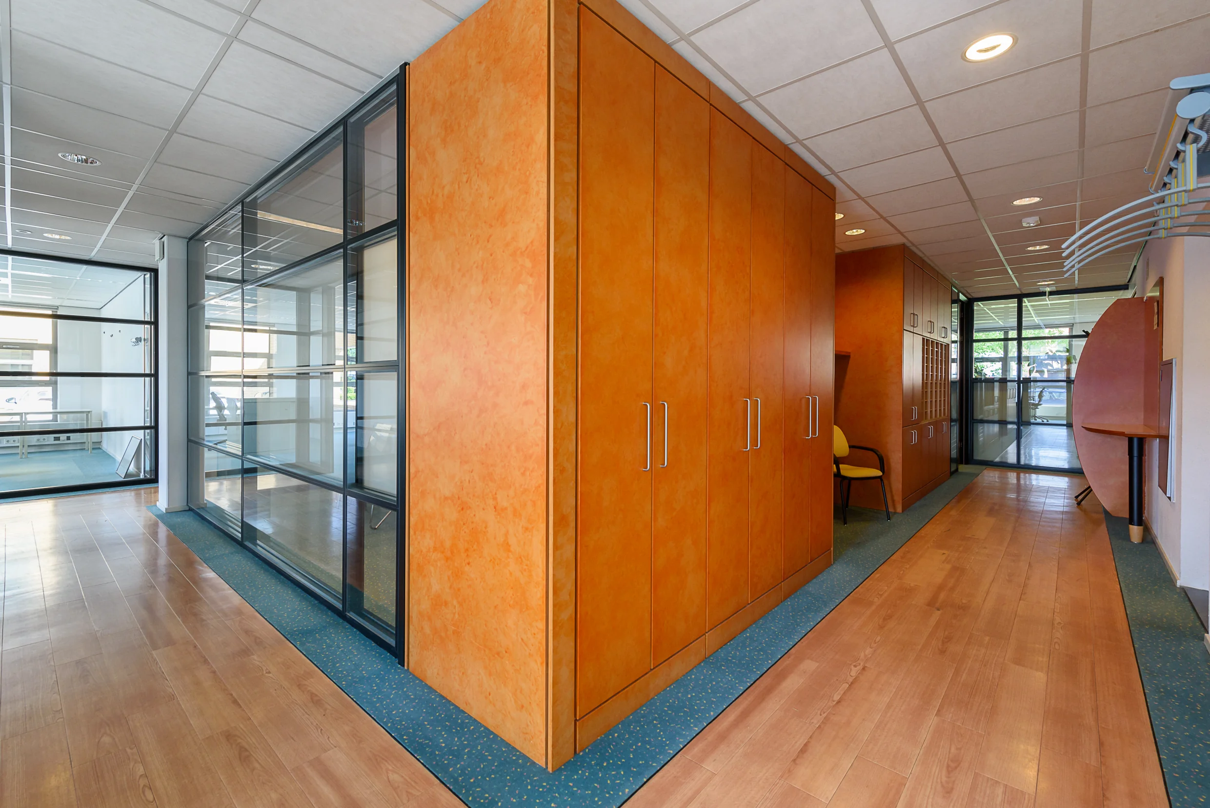 Moderne kantoorruimte in Capelle aan den IJssel met houten vloer, oranje wandkasten en glazen scheidingswanden.