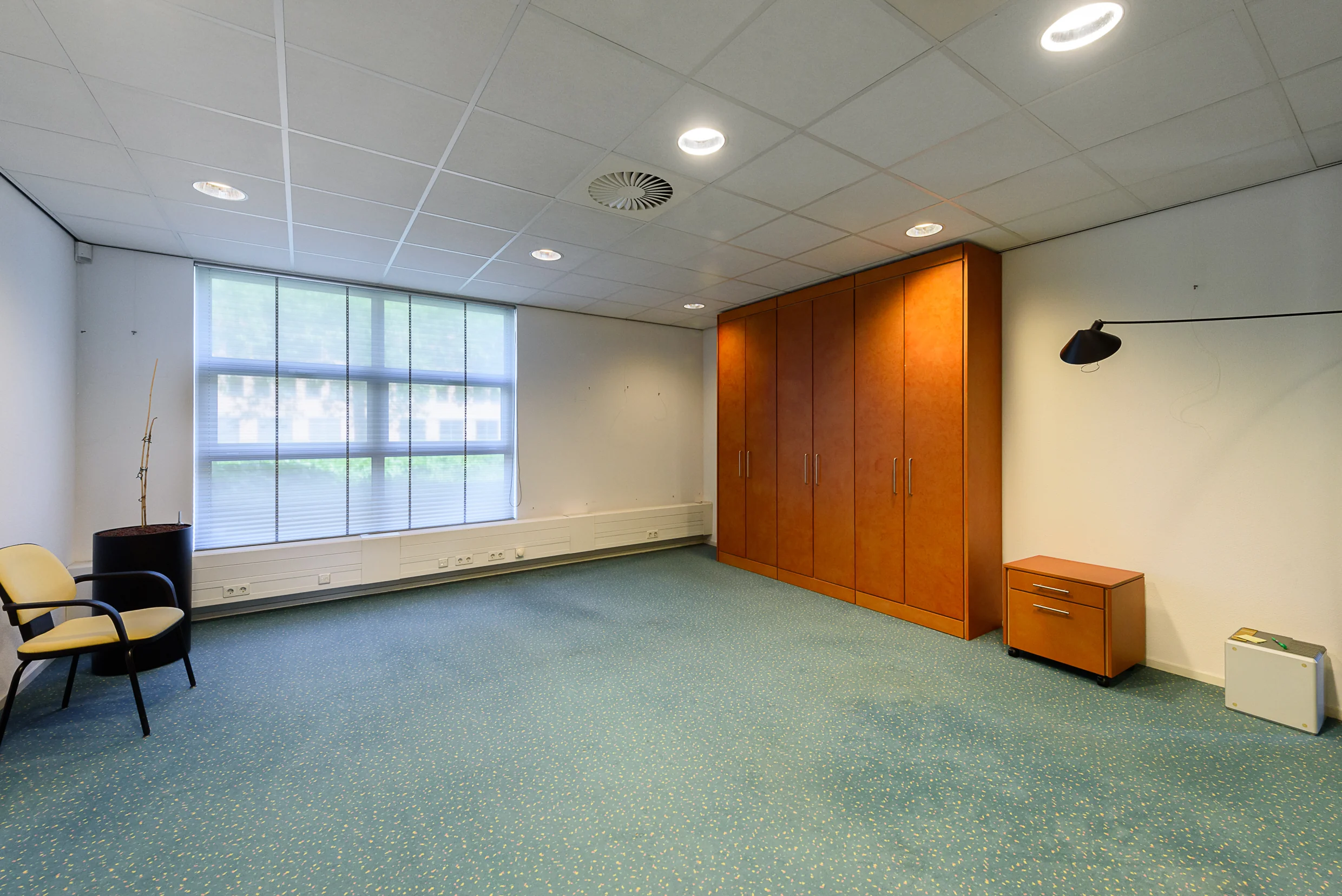 Lege kantoorruimte in Capelle aan den IJssel met ingebouwde houten kasten en groot raam met jaloezieën.