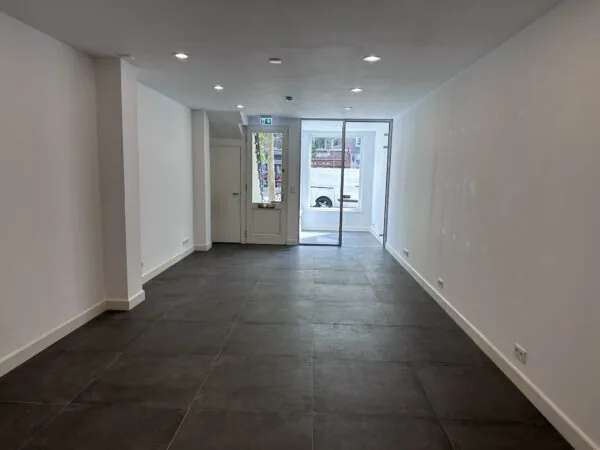 Leeg winkelpand aan de Ceintuurbaan met witte muren, donkere vloertegels en een glazen voordeur.