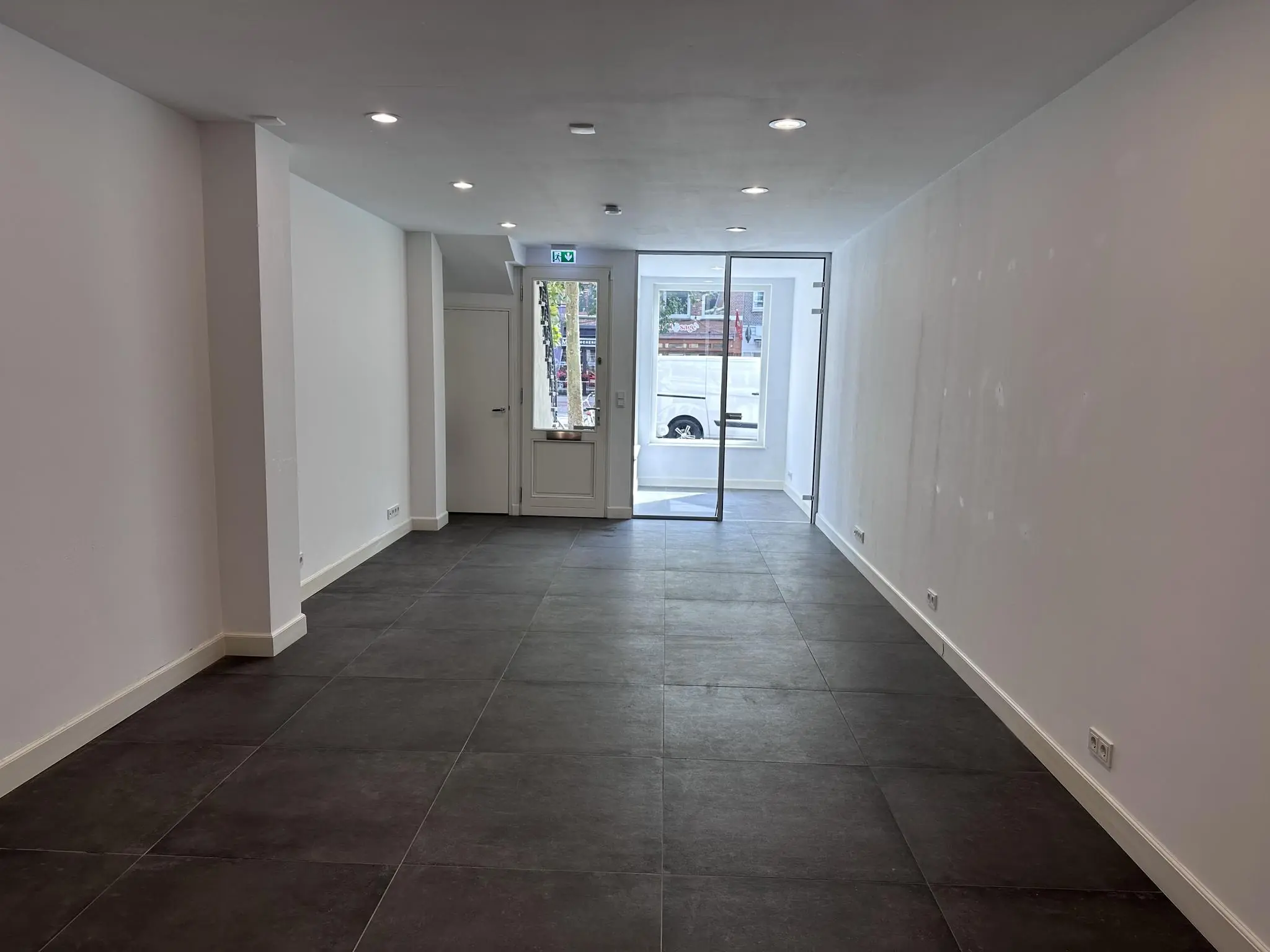 Leeg winkelpand aan de Ceintuurbaan met witte muren, donkere vloertegels en een glazen voordeur.